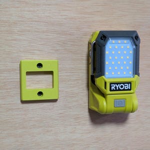 May include: A yellow and black Ryobi LED work light with a rectangular light array and a power button. A matching yellow mounting bracket is to the left. The light is on a wooden surface.