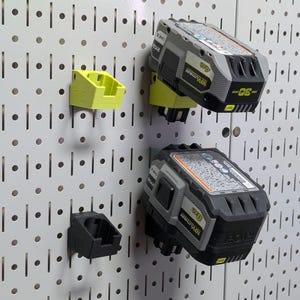 May include: A pegboard with several battery holders and power tool batteries. The holders are lime green and black. The batteries are gray and black with yellow accents. The pegboard is white.