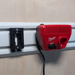 May include: A red Milwaukee M12 battery charger mounted on a white track system. The charger has a black power cord and a black mounting bracket is to the left. The charger has the Milwaukee logo and M12 printed on it.