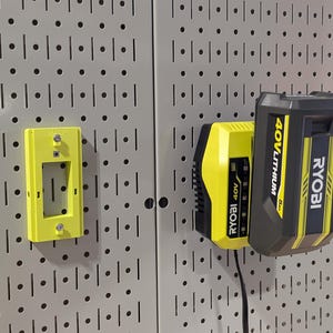 May include: A yellow and black Ryobi 40V Lithium battery and charger are mounted on a pegboard. A yellow bracket is also mounted on the pegboard. The charger is plugged in.