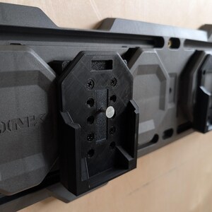 May include: A modular, dark gray wall-mounted storage system with black attachments. The system features the word "LINK" embossed on the gray panels. The black attachments appear to be designed to hold various items.