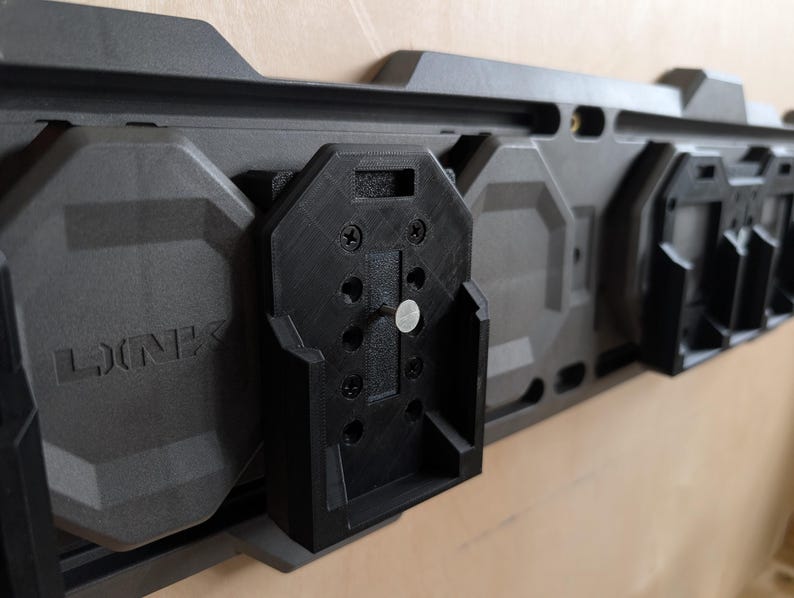 May include: A modular, dark gray wall-mounted storage system with black attachments. The system features the word "LINK" embossed on the gray panels. The black attachments appear to be designed to hold various items.