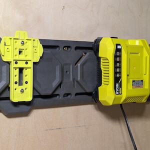 May include: A yellow and black Ryobi 40V battery charger and a yellow mounting bracket attached to a dark gray wall-mounted track system. The charger is plugged in and has a series of indicator lights.