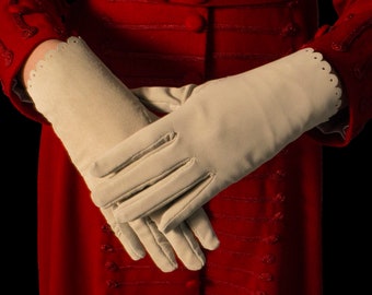 May include: A pair of white gloves with scalloped edges, worn by a person in a red jacket.