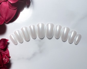 May include: A set of ten oval-shaped, white, pearl-like press-on nails.