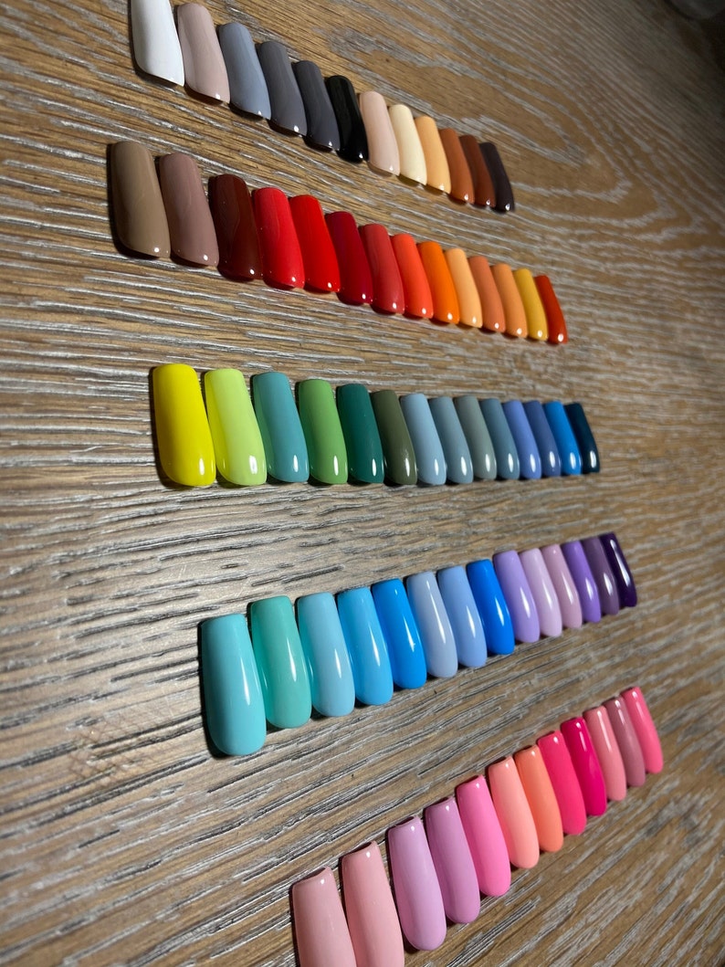 May include: A set of 50 colorful nail tips in various shades of white, gray, brown, red, orange, yellow, green, blue, purple, and pink. The tips are arranged in rows on a wooden surface.