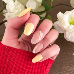 May include: Close-up of a hand with five nails painted in a light yellow color and a nude color with black and white abstract designs.