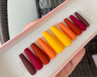 May include: A set of ten false nails in a gradient of fall colors, from deep burgundy to bright yellow. The nails are arranged in a box with a pink interior.