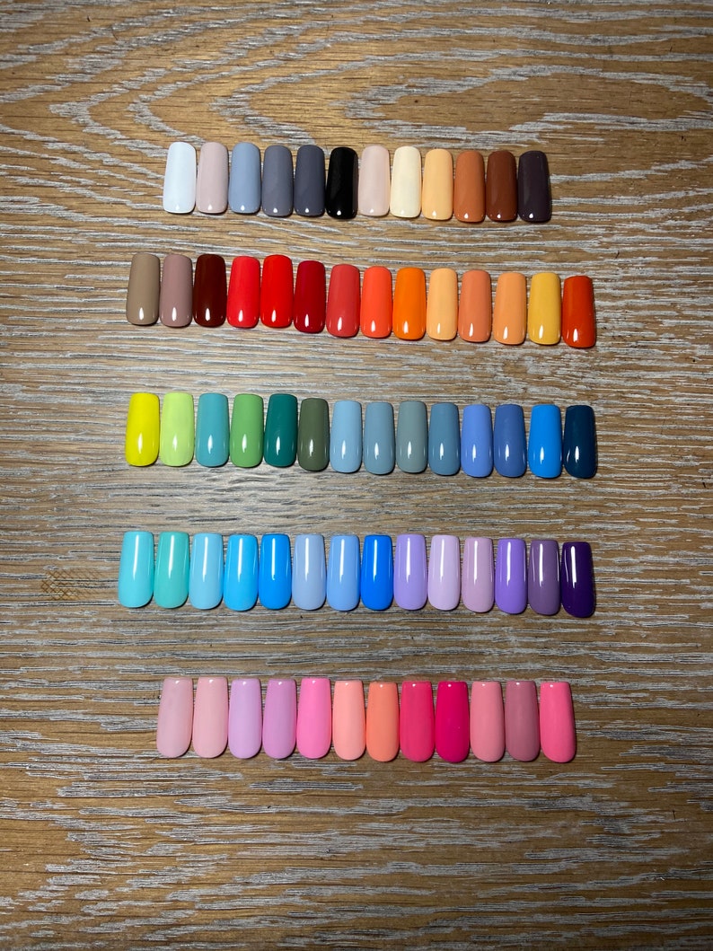 May include: A collection of 50 different colored nail polish colors displayed in rows on a wooden surface. The colors range from light to dark and include shades of red, orange, yellow, green, blue, purple, and pink.