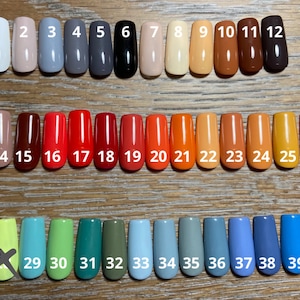 May include: Forty different colored nail polish samples displayed in rows on a wooden surface. The samples are numbered 1 through 40.
