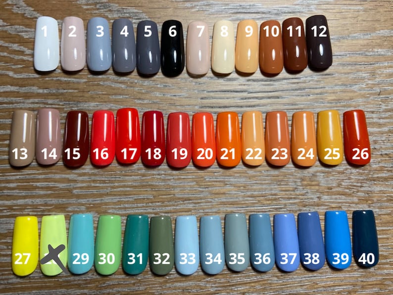 May include: Forty different colored nail polish samples displayed in rows on a wooden surface. The samples are numbered 1 through 40.