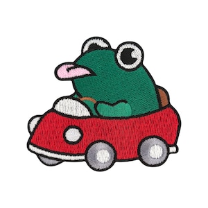 Könnte beinhalten: Ein gestickter Aufnäher mit einem grünen Frosch, der ein rotes Auto mit weißen Rädern fährt. Der Frosch hat eine rosa Zunge herausgestreckt und große schwarze Augen.