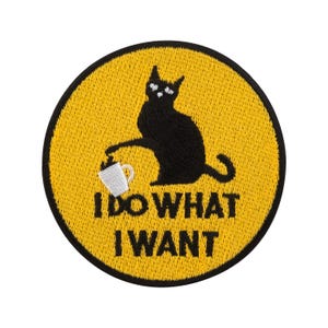 Könnte beinhalten: Runder, gestickter Aufnäher mit einer schwarzen Katze, die eine Kaffeetasse auf gelbem Hintergrund hält. Der Text "I DO WHAT I WANT" ist schwarz. Der Aufnäher hat einen schwarzen Rand.