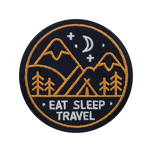 May include: Round, navy blue patch with a gold border and camping-themed design. The design includes mountains, trees, a tent, a crescent moon, stars, and the words "EAT SLEEP TRAVEL" in white.