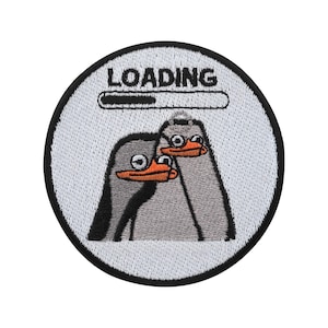 Puede incluir: Parche bordado redondo con borde negro, con dos pingüinos de dibujos animados con picos y gafas naranjas. La palabra "LOADING" está encima de una barra de progreso. Fondo blanco.