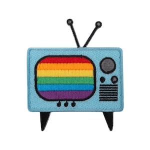 Pode incluir: Um patch bordado azul claro em forma de televisão retro. O ecrã exibe um design de arco-íris. O patch tem antenas, pernas e detalhes pretos.