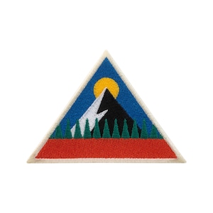 Könnte beinhalten: Gestickter Aufnäher in Dreiecksform mit einer Berglandschaft. Das Design umfasst einen schwarzen Berg, einen weißen Berg, eine gelbe Sonne, grüne Bäume, einen blauen Himmel und eine rote Basis. Der Aufnäher hat einen weißen Rand.