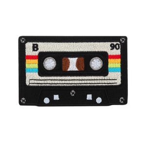 May include: Black and white cassette tape patch with rainbow stripes and the number 90. The patch has a retro design, with the letter "B" visible. The patch is rectangular and has a stitched border.