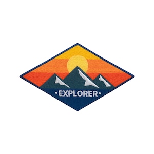 Może przedstawiać: Haftowana naszywka w kształcie rombu przedstawiająca krajobraz górski o zachodzie słońca. Projekt zawiera kolory pomarańczowy, żółty i granatowy, z napisem "EXPLORER" haftowanym na biało.