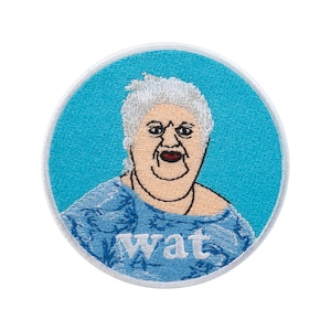 Op de afbeelding: Ronde geborduurde patch met een cartoonafbeelding van een vrouw met wit haar en een verbaasde uitdrukking. De vrouw draagt een blauwe top en het woord "wat" is in het wit geborduurd. De patch heeft een blauwe achtergrond en een witte rand.