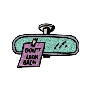 Könnte beinhalten: Ein grüner Rückspiegel mit einem lila Zettel, auf dem "Schau nicht zurück" steht.