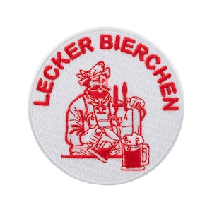 Puede incluir: Un parche redondo blanco con texto y un diseño bordados en rojo. El texto "LECKER BIERCHEN" está en un arco. El diseño muestra a un hombre con bigote, sosteniendo grifos de cerveza y una jarra de cerveza. El parche es para ropa o accesorios.
