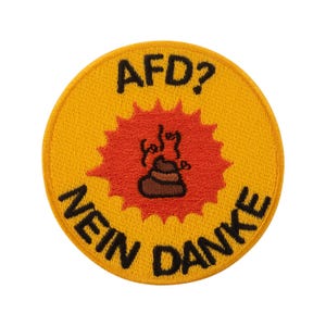 Könnte beinhalten: Runder gelber Aufnäher mit schwarzem Text „AFD? NEIN DANKE“. Der Aufnäher hat ein rotes Stern-Design mit einem braunen Kackhaufen-Emoji in der Mitte.