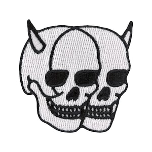 Puede incluir: Parche blanco bordado de dos calaveras con cuernos, enfrentadas. Las calaveras están delineadas en negro y tienen ojos negros.