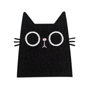 Puede incluir: Parche de fieltro negro con forma de cara de gato con ojos blancos y nariz rosa.