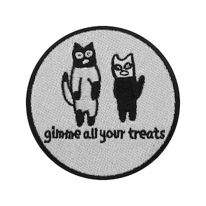 Op de afbeelding: Ronde geborduurde patch met twee gestileerde katten in zwart en wit. De katten staan op een lichtgrijze achtergrond, omgeven door een zwarte rand. De tekst "gimme all your treats" staat in kleine letters onder de katten.