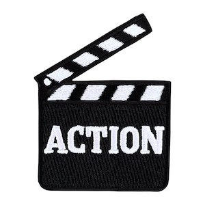 Puede incluir: Parche bordado en blanco y negro de una claqueta con la palabra "ACCIÓN" en letras blancas.