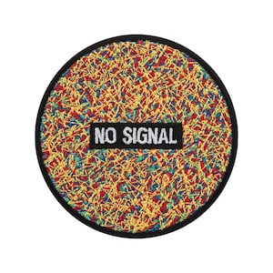 以下が含まれることがあります： 黒い縁取りの丸い刺繍パッチ。パッチは、黄色、赤、青、緑のカラフルでテクスチャード加工されたデザインが特徴です。 白で「NO SIGNAL」という言葉が入った黒い長方形がパッチの中央に配置されています。