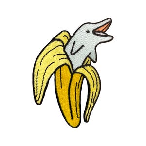 May include: A yellow banana with a grey dolphin peeking out of the top. The dolphin is facing forward with its mouth open.