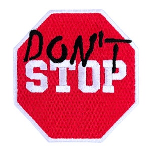 May include: Red octagonal stop sign with a white border and white text that says "DON'T STOP" in black lettering.
