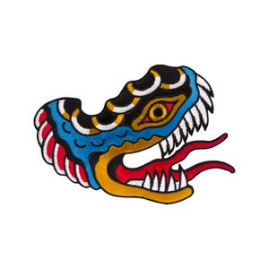 Può includere: Un toppa ricamata colorata di una testa di serpente con la bocca spalancata, che mostra denti affilati. Il serpente è nero, blu, giallo, rosso e bianco.