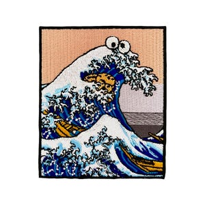 Op de afbeelding: Een geborduurde patch met een blauwe en witte golf met een gele boot en een cookie monster gezicht met oogjes. De achtergrond is perzikkleurig.