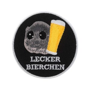 Może przedstawiać: Haftowana naszywka z szarym gryzoniem i żółtym kuflem piwa na czarnym tle. Tekst "LECKER BIERCHEN" jest haftowany na biało. Zabawny design.
