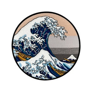 May include: An embroidered patch featuring a large wave in blue and white, with a traditional Japanese design. The wave is breaking over a small boat with a mountain in the background.