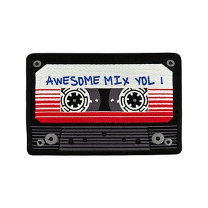 May include: Embroidered patch in the shape of a cassette tape. The patch features a black border, a white top section with the text "AWESOME MIX VOL 1" in blue, and a red stripe across the middle. The tape reels are gray and white.
