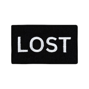 Op de afbeelding: Zwarte rechthoekige patch met witte geborduurde tekst die "LOST" zegt.