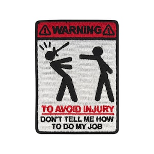 Op de afbeelding: Een wit en rood waarschuwingsbord met een zwarte stick figure illustratie. Het bord luidt "WARNING" en "TO AVOID INJURY DON'T TELL ME HOW TO DO MY JOB".