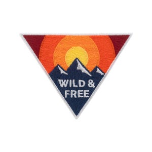 Könnte beinhalten: Gestickter Aufnäher in Dreiecksform mit weißem Rand. Das Design zeigt eine dunkelblaue Bergkette, einen orange-gelben Sonnenuntergang und den weißen Text "WILD & FREE".