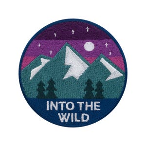 Può includere: Toppa ricamata rotonda raffigurante un paesaggio montano sotto un cielo notturno. Il design presenta montagne turchesi con dettagli bianchi, un cielo viola e rosa, una luna piena e la scritta "INTO THE WILD" in bianco su sfondo blu navy.