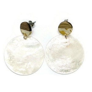 Peut inclure: Une paire de boucles d'oreilles en coquille blanche avec des accents dorés. Les boucles d'oreilles sont rondes et ont une finition lisse et polie.