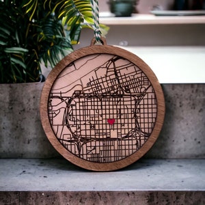 May include: A wooden ornament shaped like a circle with a map of a city inside. A red heart is in the center of the map.