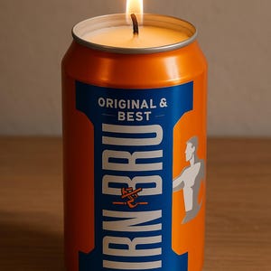 May include: A lit candle in an orange and blue IRN-BRU can. The can features the text "ORIGINAL & BEST" and a graphic of a person. The candle has a white wax base.