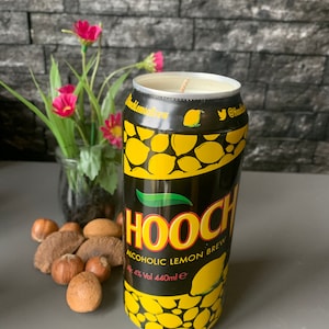 Może przedstawiać: Czarna świeca w kształcie puszki z alkoholowym napojem cytrynowym. Puszka ma żółty wzór cytryny i napis "Hooch Alcoholic Lemon Brew Alc 4% Vol 440ml e".