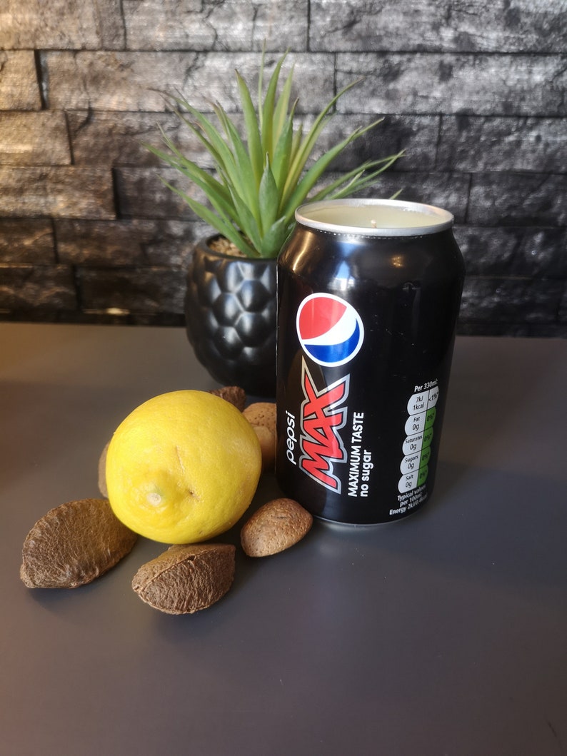 May include: A black can of Pepsi Max with the text "Maximum Taste No Sugar" on the side. The can is sitting on a gray surface with a lemon and several brown nuts.