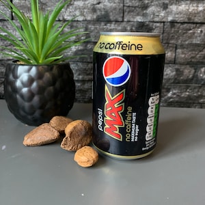 May include: A black can of Pepsi Max with a gold top. The can has the text "no caffeine" and "maximum taste" printed on it. The can is sitting on a gray surface.