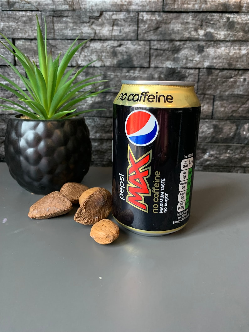 May include: A black can of Pepsi Max with a gold top. The can has the text "no caffeine" and "maximum taste" printed on it. The can is sitting on a gray surface.